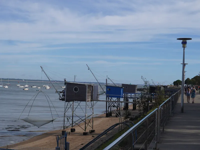 Carrelets — square-net fishing huts on stilts — along the seafront promenade, with sailing boats at anchor
